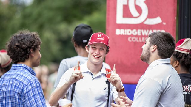 Student holding up pointer fingers with BC hat on surrounded by other students