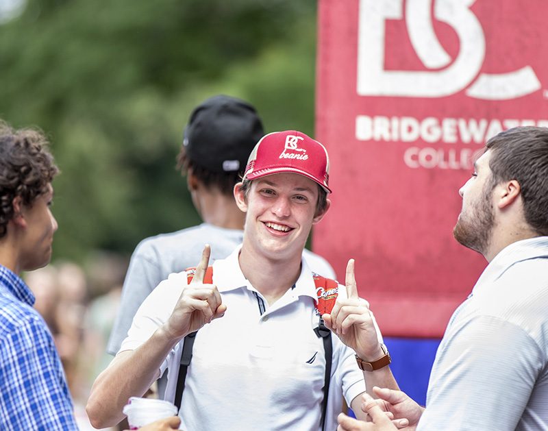 Student holding up pointer fingers with BC hat on surrounded by other students