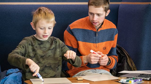 Teacher education program student sitting with second grader writing on white boards