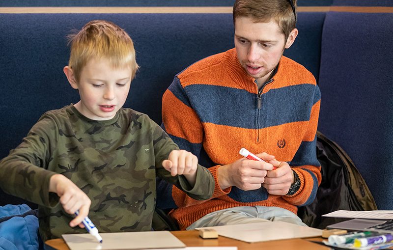 Teacher education program student sitting with second grader writing on white boards