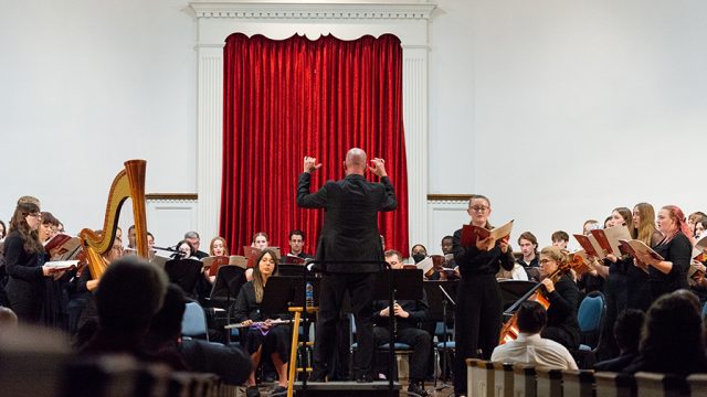 Music director standing in front large music ensemble during performance