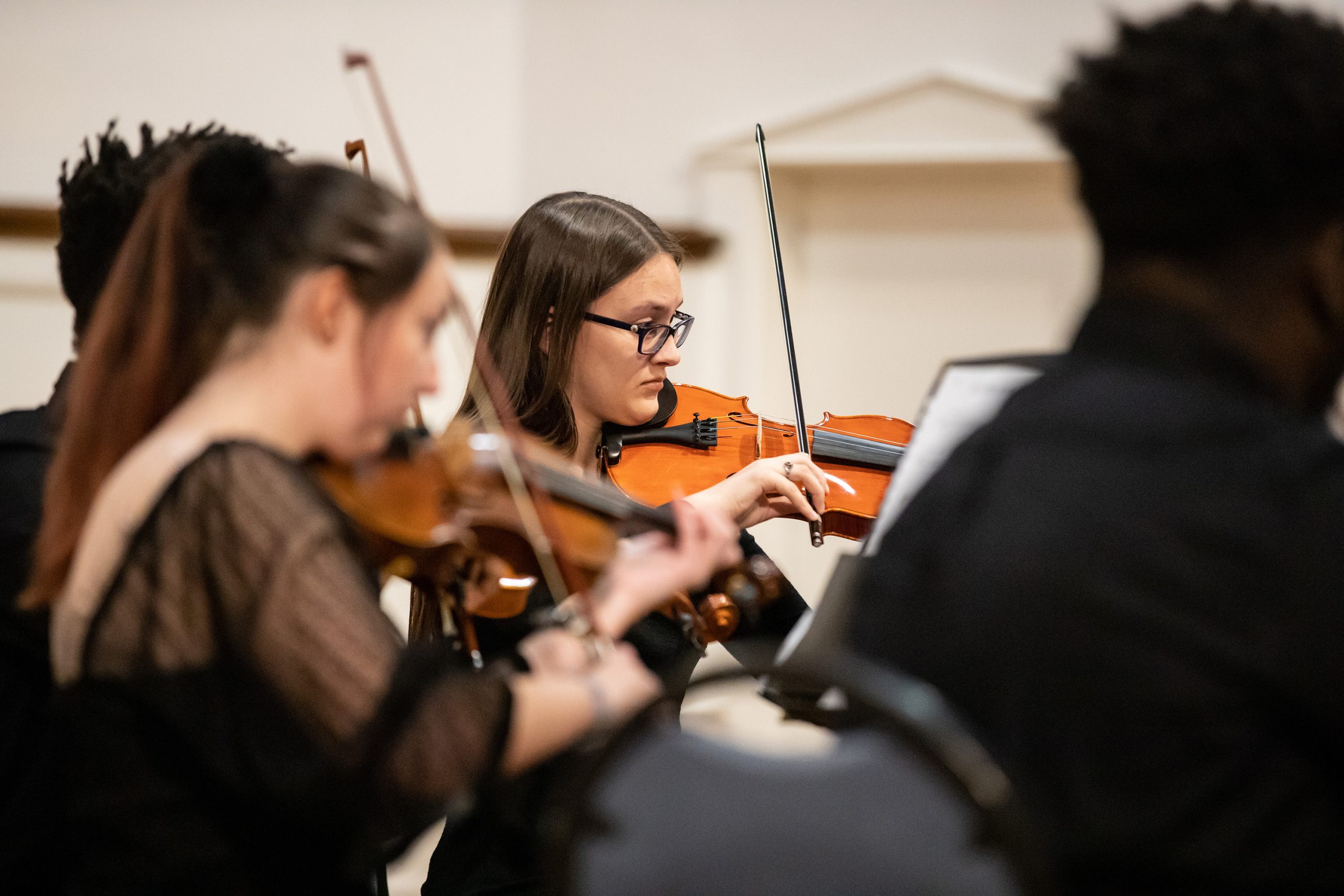 Student playing violin during performance surrounded by other players.