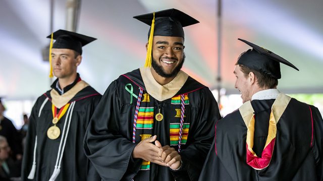 3 graduates at Commencement one smiling for the camera