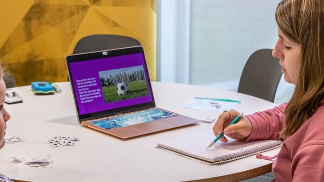 Student in teacher education program teaching a student while sitting at a table with laptop