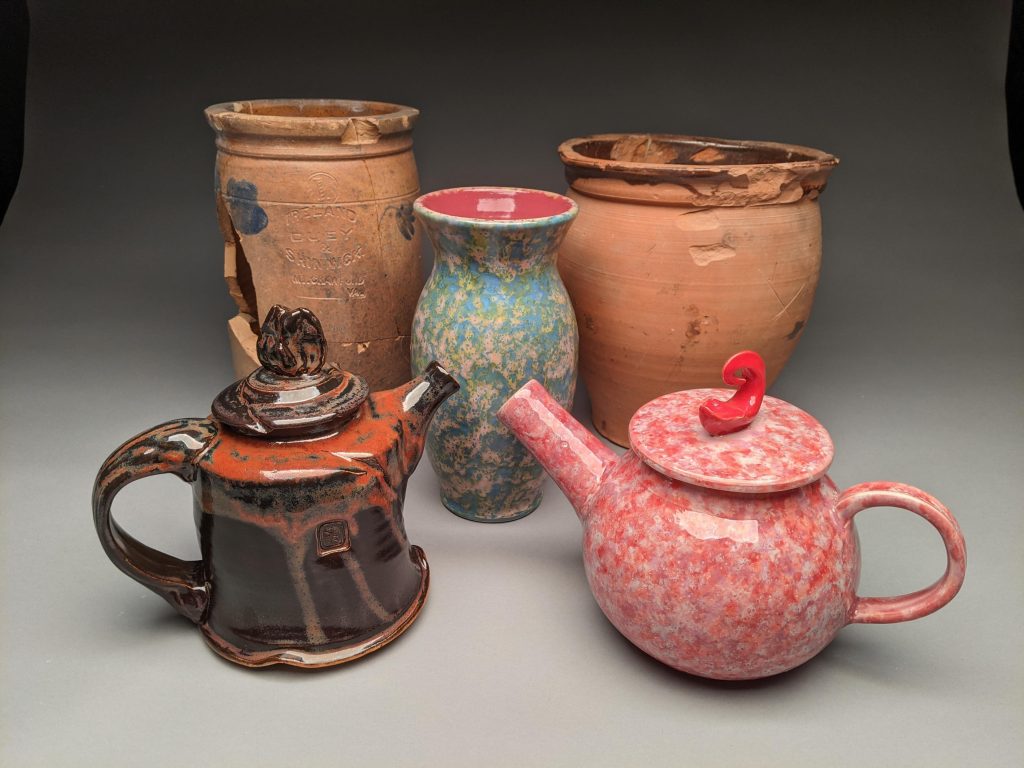 Five pieces of pottery. The back three are vases, two of which are worn and cracked and one is blue, green and pink. In front are two tea pots. One is brown and one is pink.