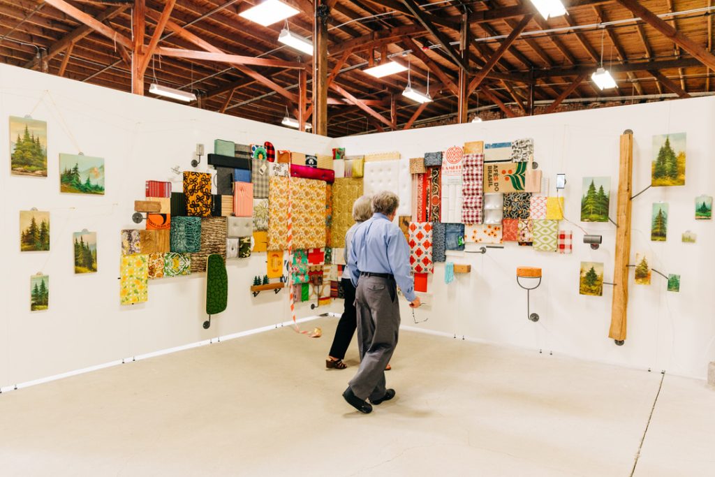 Two people walk through a color art display of textiles.