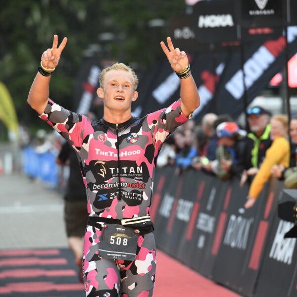 Grant Heidebrecht crossing the finish line of Ironman Alaska smiling and holding two peace signs in the air