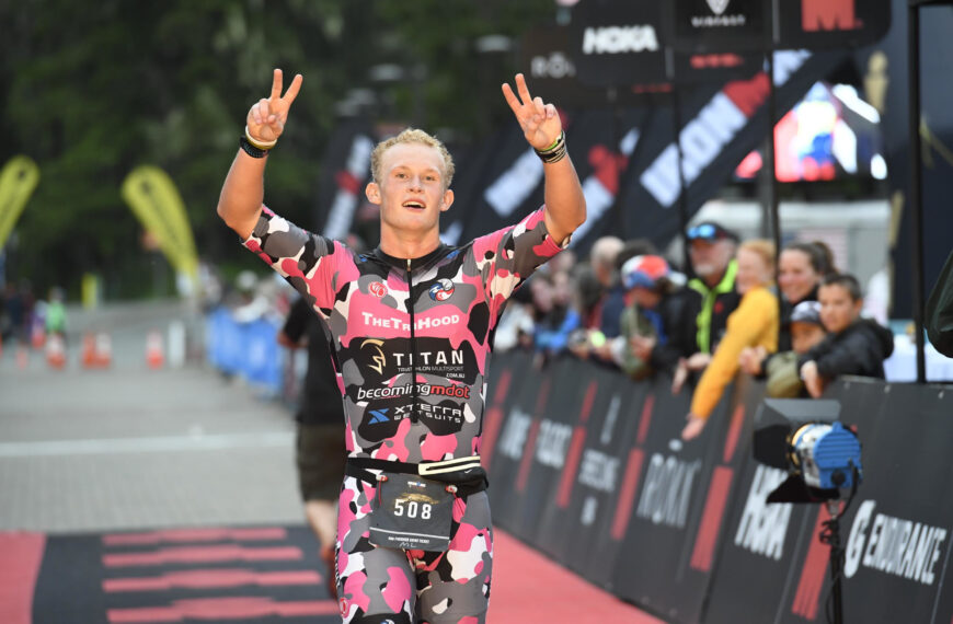 Grant Heidebrecht crossing the finish line of Ironman Alaska smiling and holding two peace signs in the air