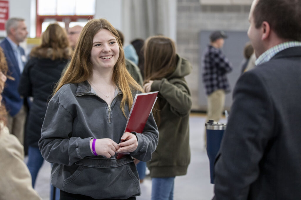 Female student smiling holding red folder talking to Bridgewater professor
