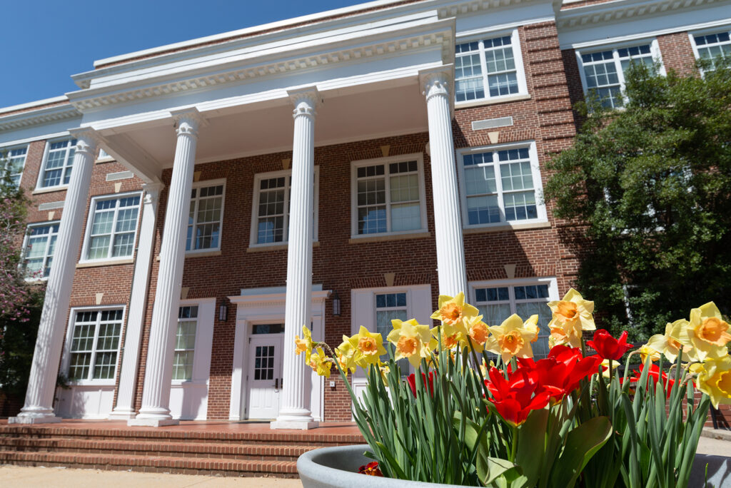 The exterior of Bowman Hall in the daytime with yellow and red flowers in front of it