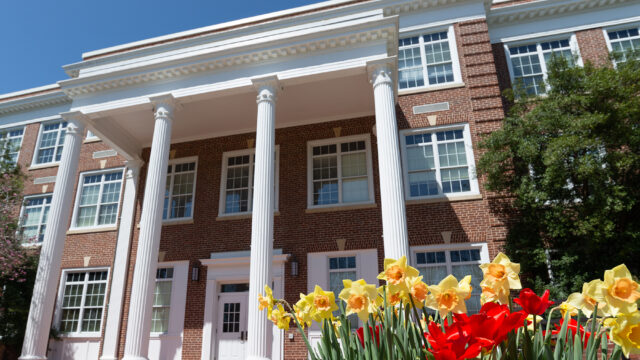 The exterior of Bowman Hall in the daytime with yellow and red flowers in front of it