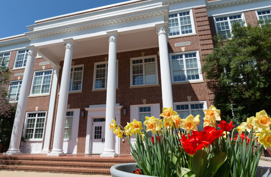 The exterior of Bowman Hall in the daytime with yellow and red flowers in front of it