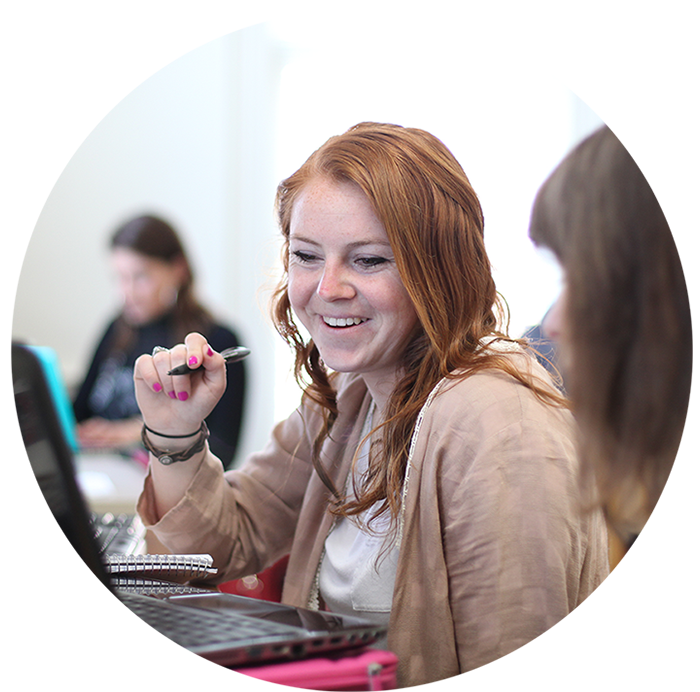 Female student smiling while looking at computer and holding a pen in her right hand 