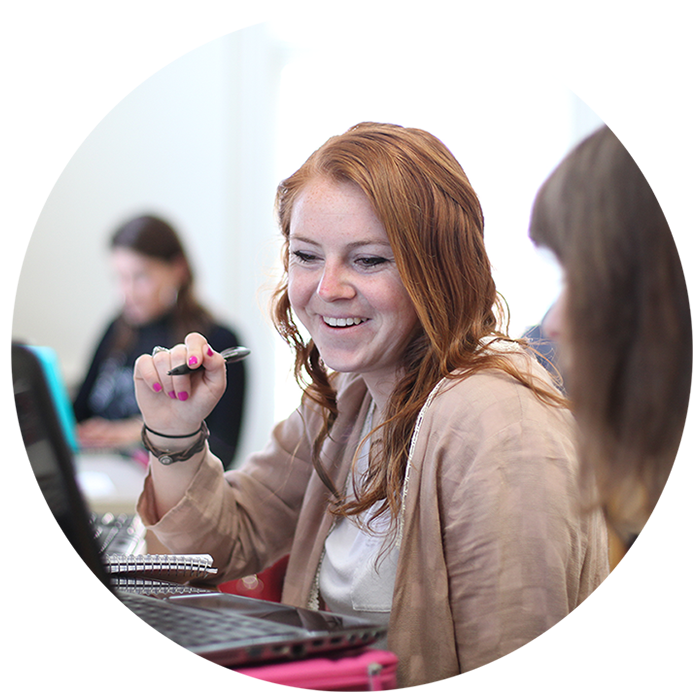 Female student smiling while looking at computer and holding a pen in her right hand