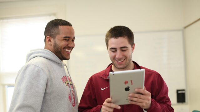 One student holding an iPad while another student looks over his shoulder