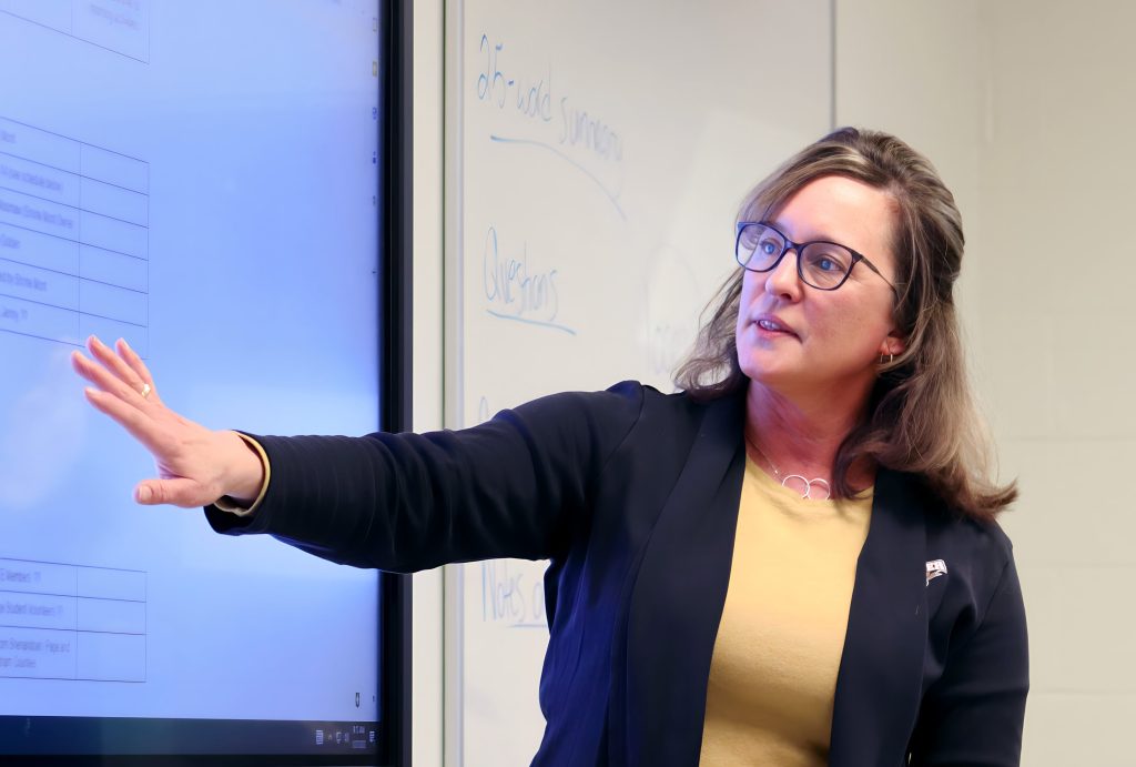 Secondary education professor gestures towards the screen to bring attention to important parts of the class syllabus. 