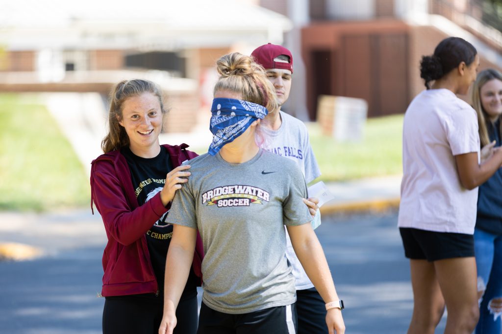 Student helping guide another student with a blind fold on her face during an outdoor class activity. 