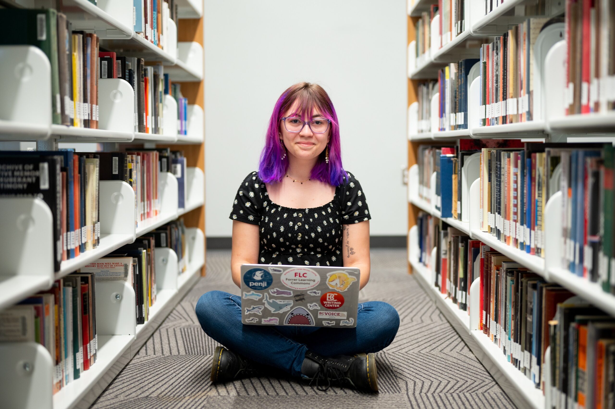 Mackenzie Hammack sitting on the floor between two bookcases with a laptop in her lap