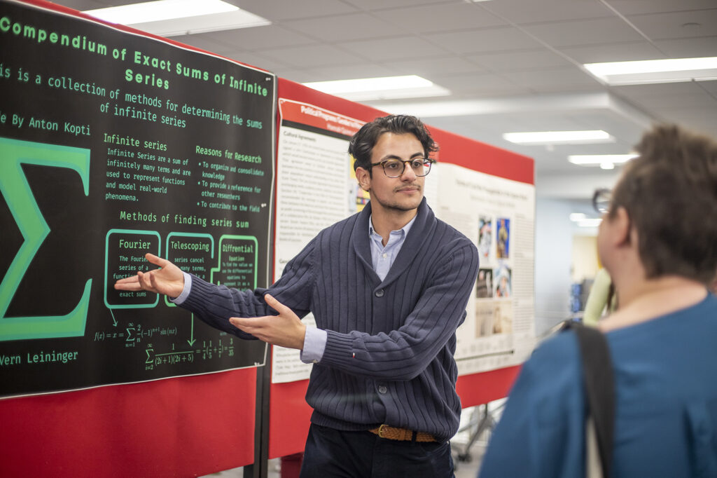 Student speaking to someone with hands pointed to poster presentation next to him 