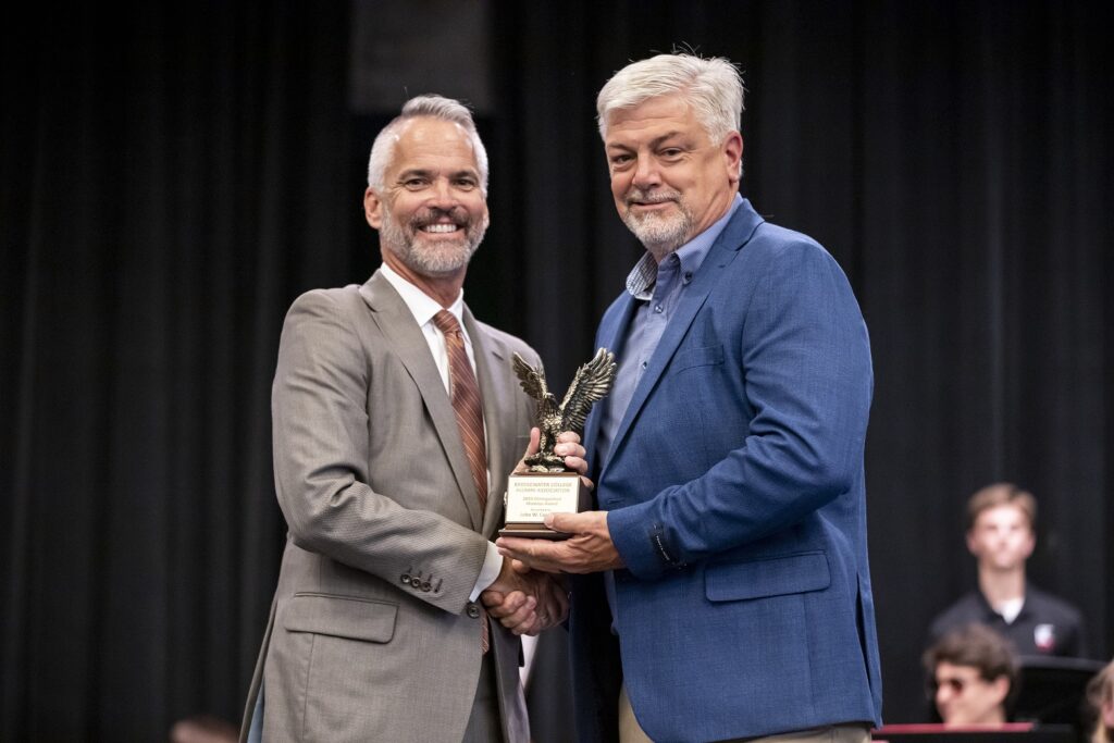 Two men smiling and shaking hands while accepting an award.