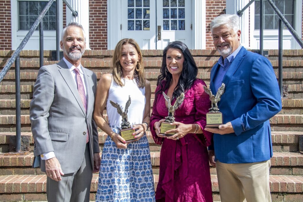 Two men and two women pose for a photo holding trophies and smiling.