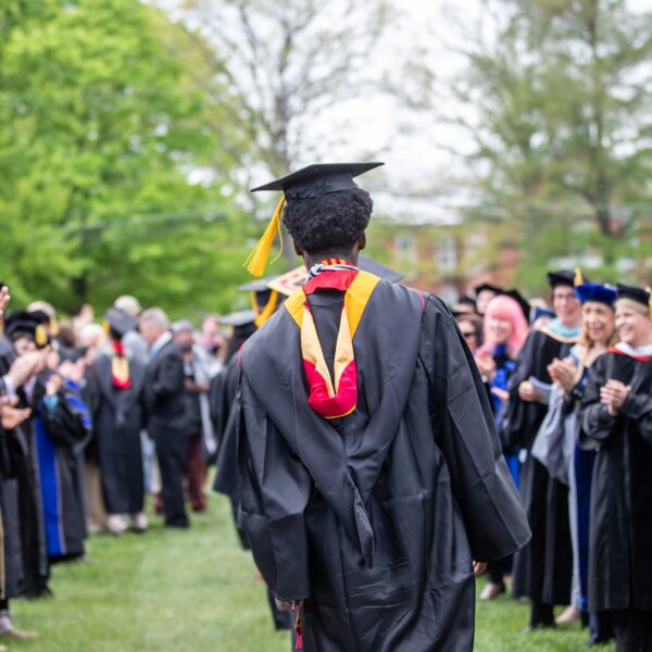 A student in a graduation cap and gown walks through an echelon of professors also in graduation regalia