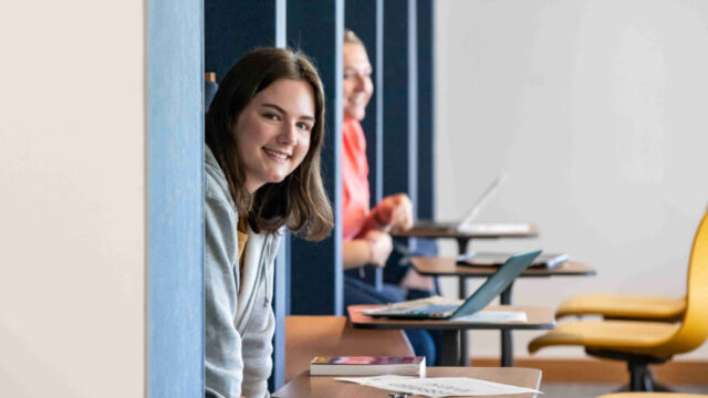 Girl sitting at a desk peaking her head out from behind a wall