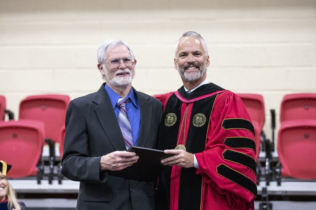 Stephen Baron and President David Bushman smiling together on stage in their academic regalia.