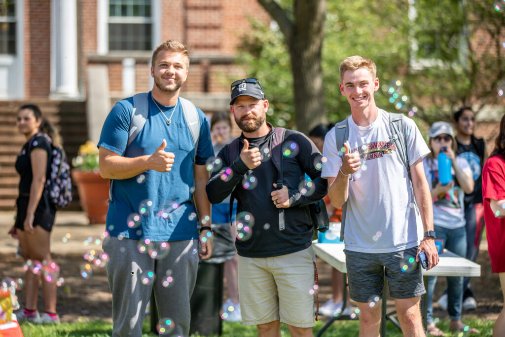 Group of 3 men looking at the camera giving thumbs up with bubbles blurred in the foreground
