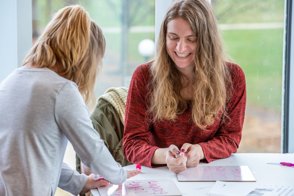 A teacher education student looks on as a local elementary school student practices adding large numbers on her whiteboard.