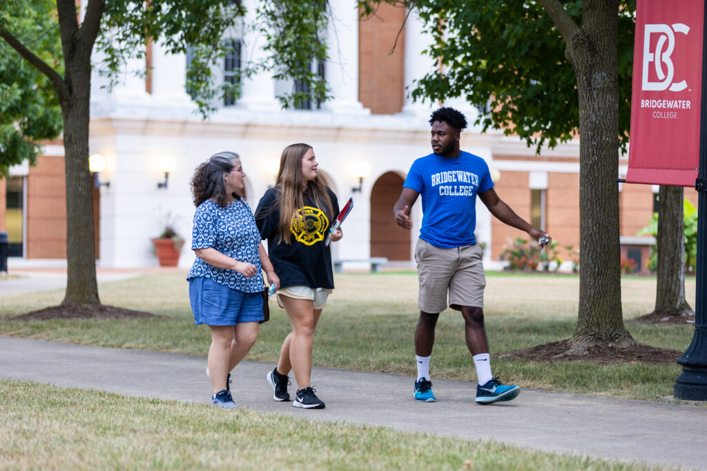 A Bridgewater employee wearing a blue Bridgewater College t-shirt taking a prospective student and her mom on a campus tour