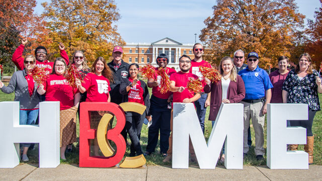 Large group of employees pose for a photo in front of letters that spell home with B-C to replace the O