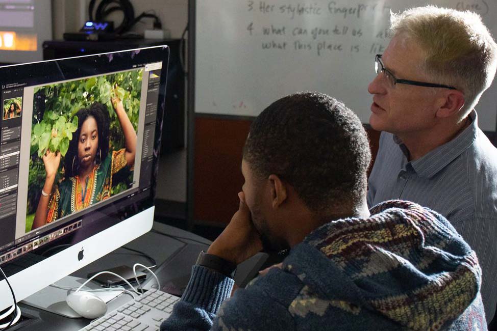 Two people looking at large computer screen with photo of a woman on it