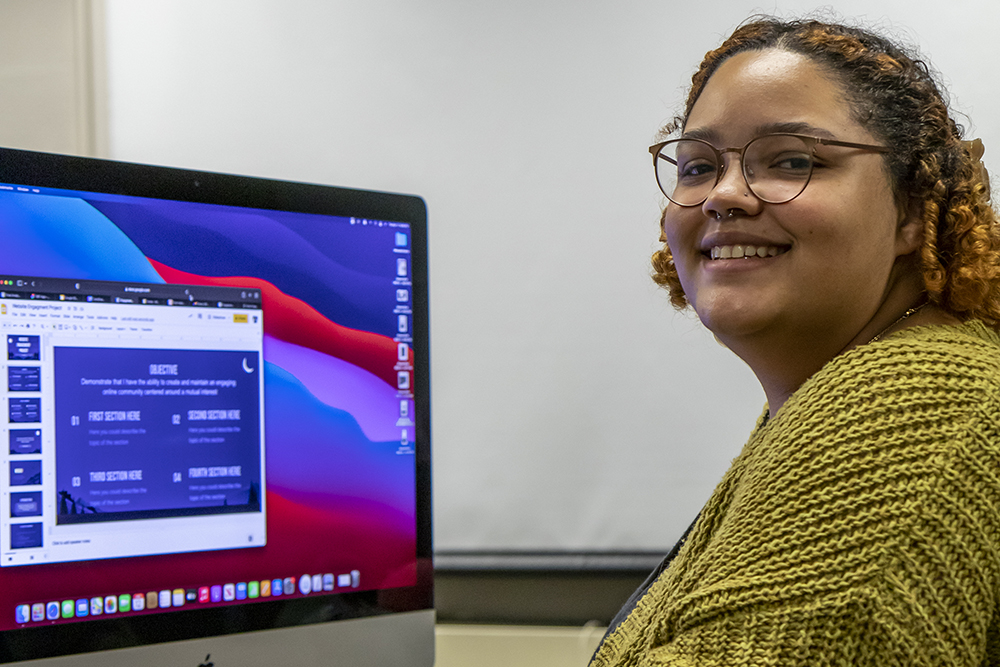 Girl smiling at camera with computer in the background