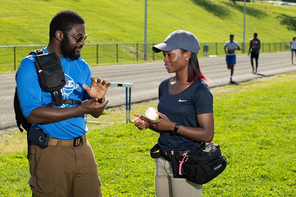 Athletic trainers talking to each other with athletes running on the track in the background