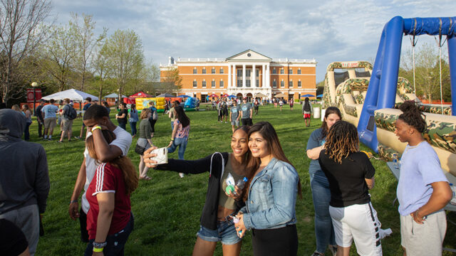 Students posing for a selfie during spring fest with McKinney Hall in the background surrounded by other students