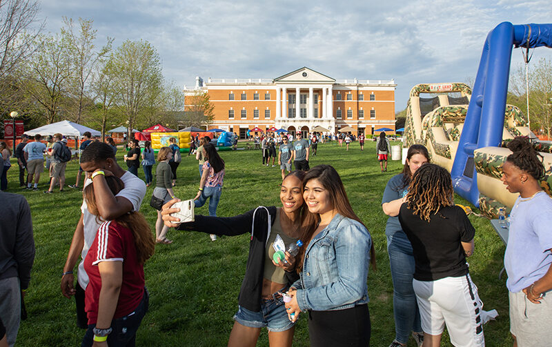 Students posing for a selfie during spring fest with McKinney Hall in the background surrounded by other students