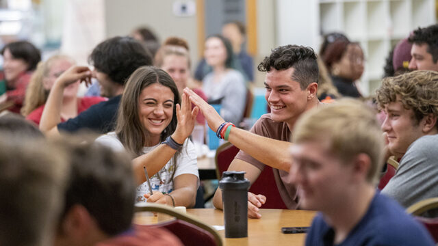 Two student high fiving in the dining hall surrounded by other students