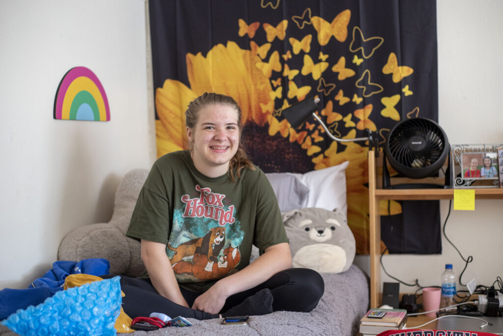 Student sitting on a bed in her dorm room with butterfly canvas on the wall
