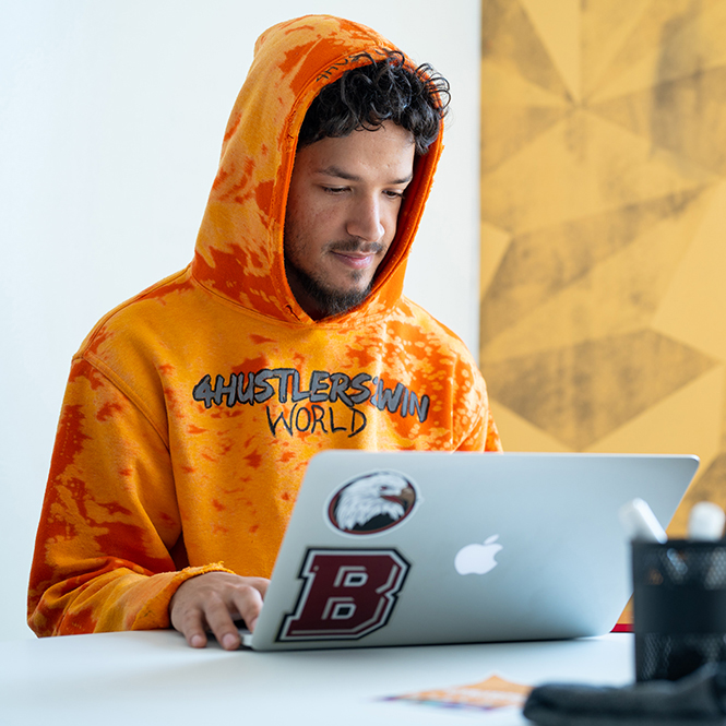 Student in orange hoodie working on laptop