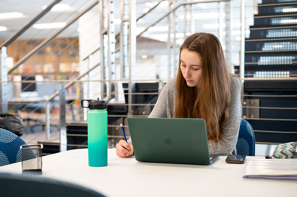 Student working at a table with a green laptop open