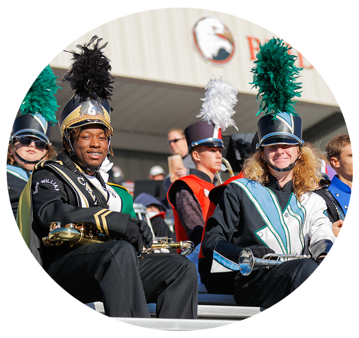 Marching band members sitting in the football stands smiling for the camera