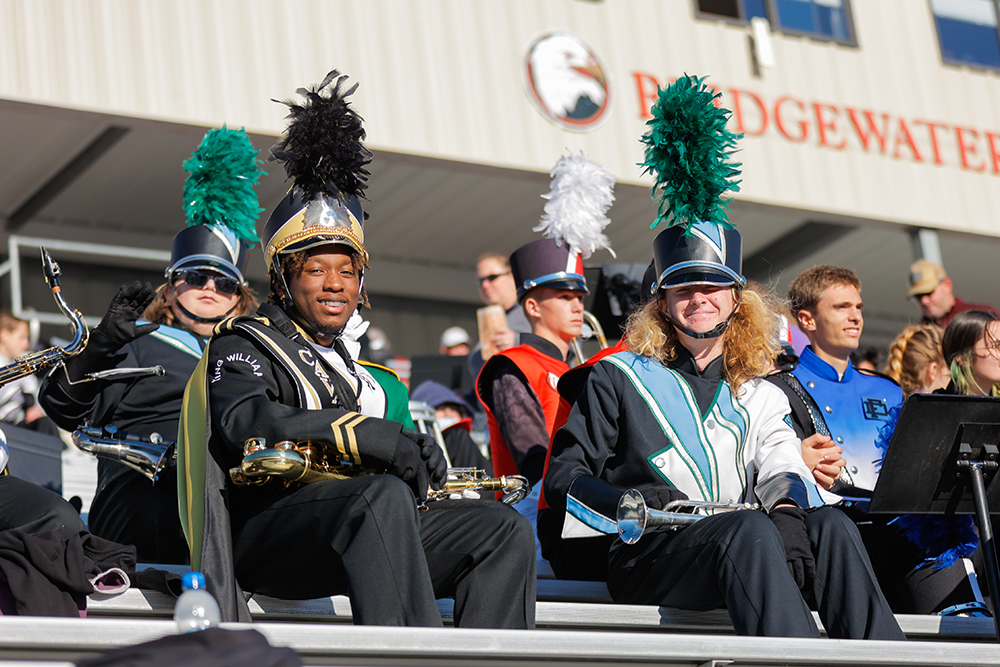 Marching band members sitting in the football stands smiling for the camera