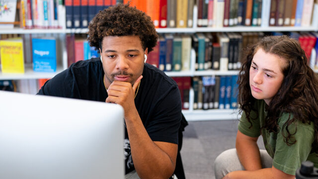Students looking at a computer screen in the F-L-C with a bookshelf behind them
