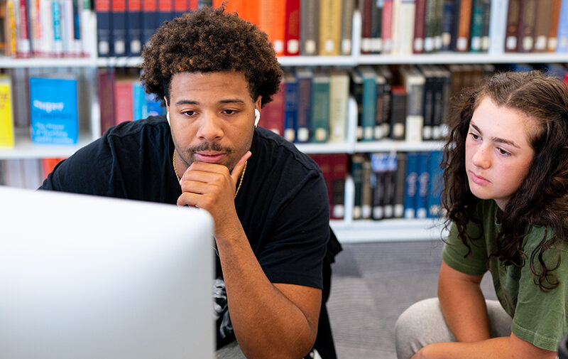 Students looking at a computer screen in the F-L-C with a bookshelf behind them