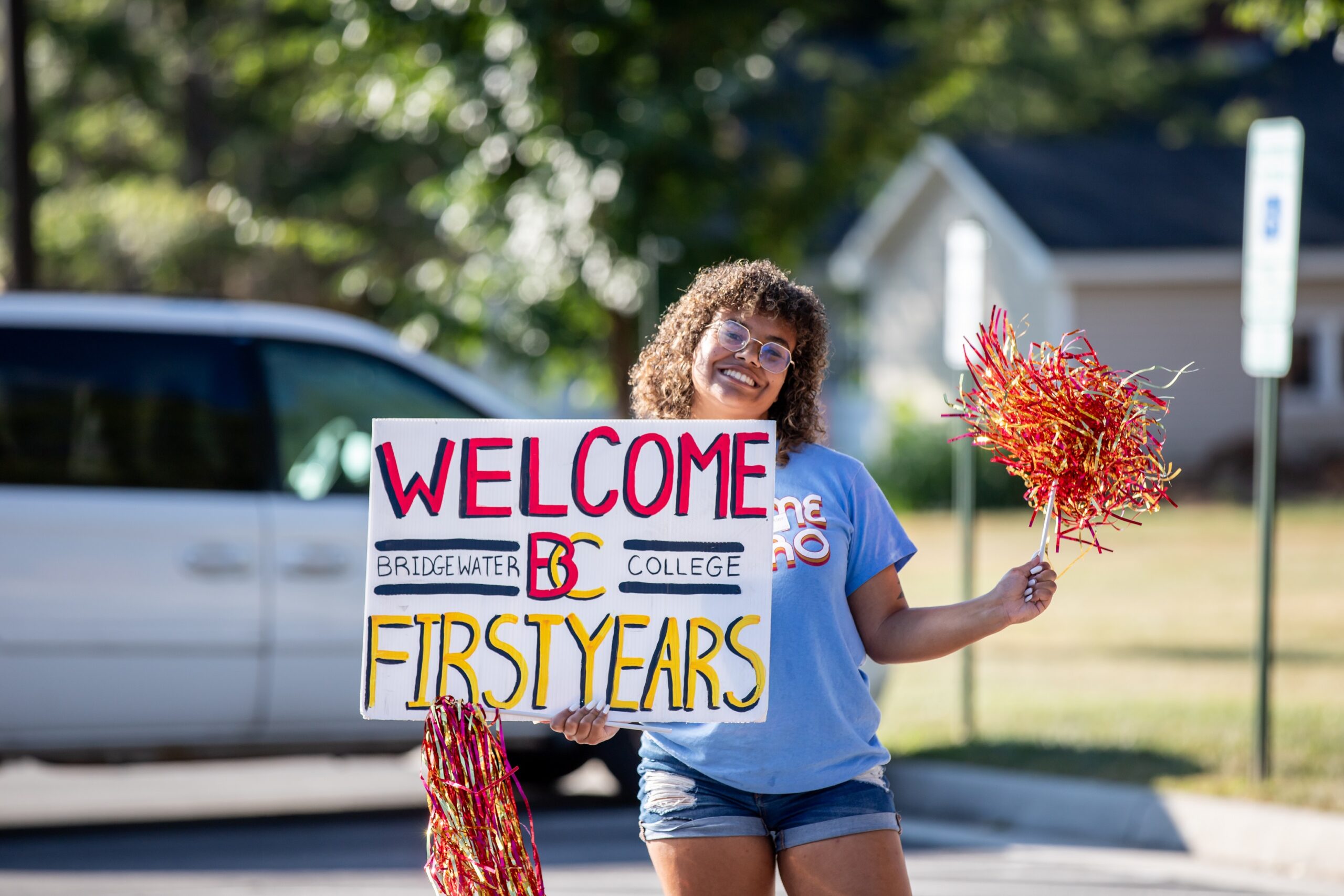 A female student holding a sign that says welcome B-C first years. In her other hand is a pompom