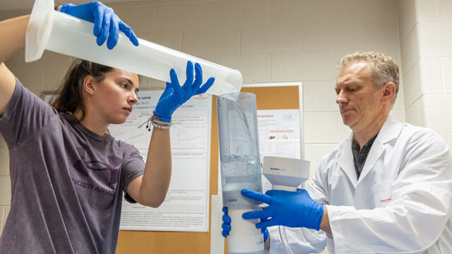 Student pouring a liquid into a tube a professor is holding for a summer research project