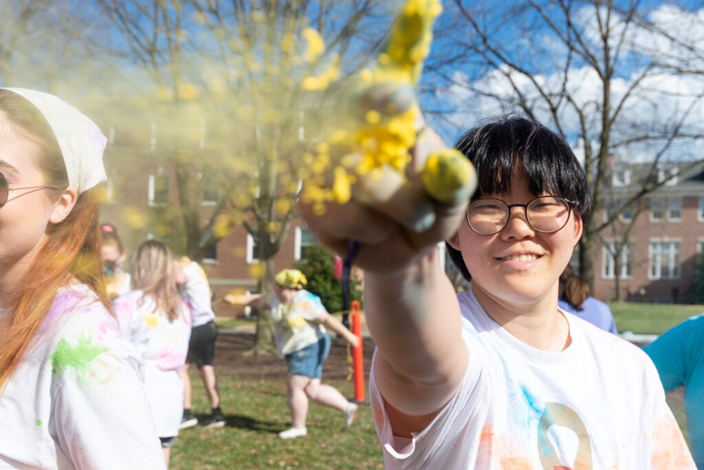 A student looks into the camera pointing upwards with yellow glitter falling off their hand.