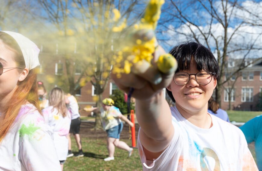 A student looks into the camera pointing upwards with yellow glitter falling off their hand.