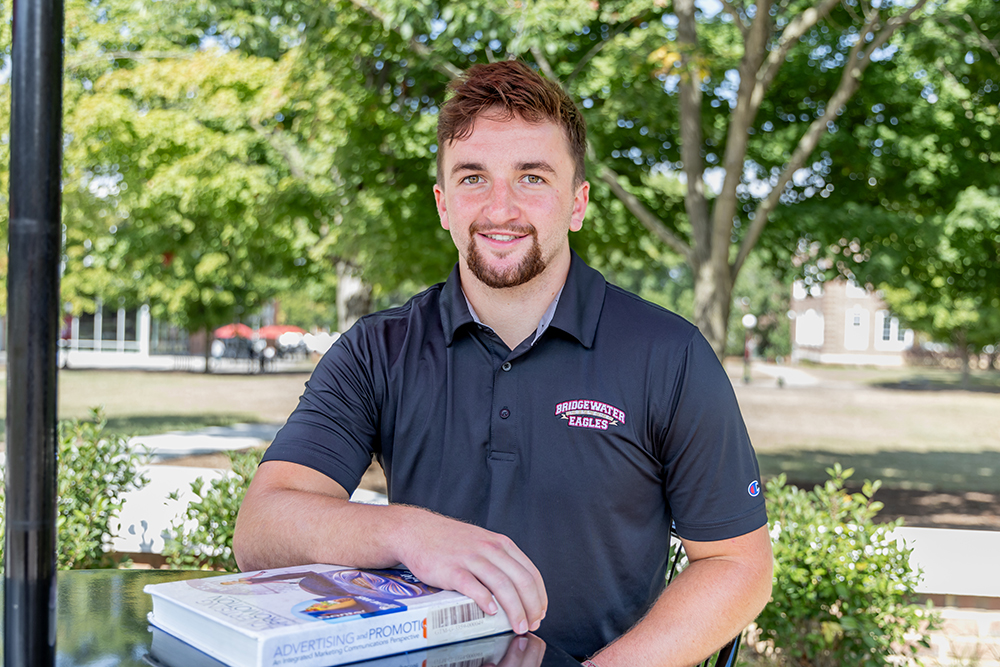 Student smiling for camera with his arm over a book